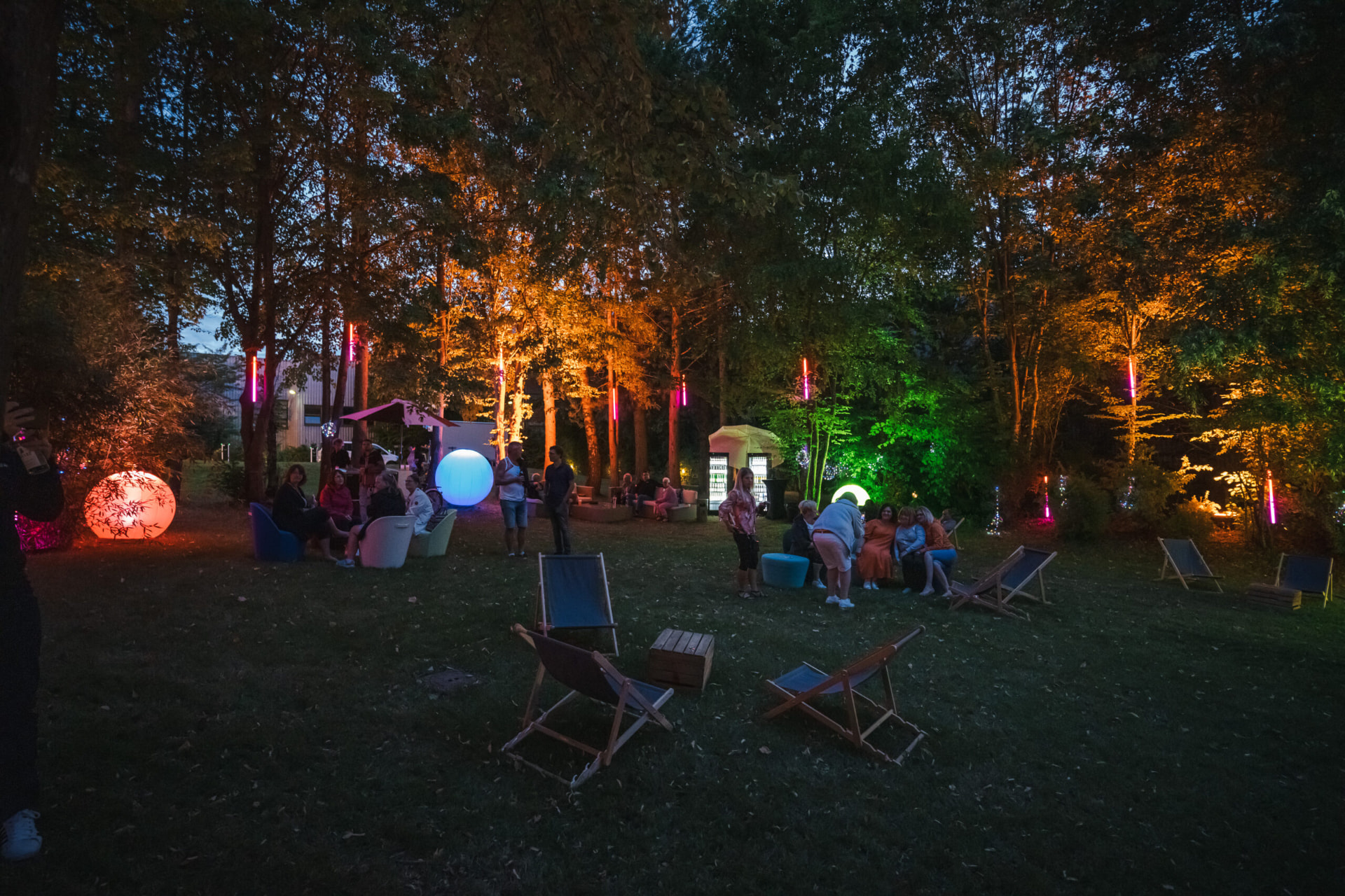Sommerfest am Abend mit farbig beleuchteten Bäumen und Liegestühlen